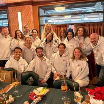 A large group of smiling people posing together wearing matching white Social Impact Hub hoodies at a dinner event
